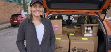 white woman standing beside a orange trunk open with cardboard boxes
