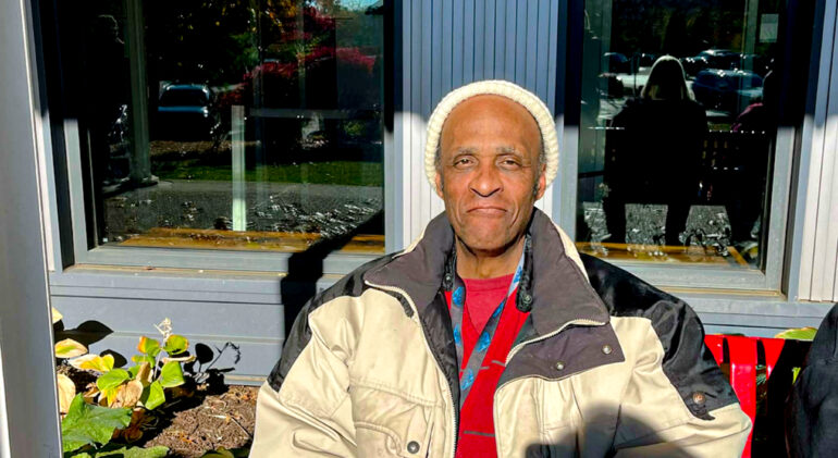 black man smiling wearing a tan jacket and white shirt