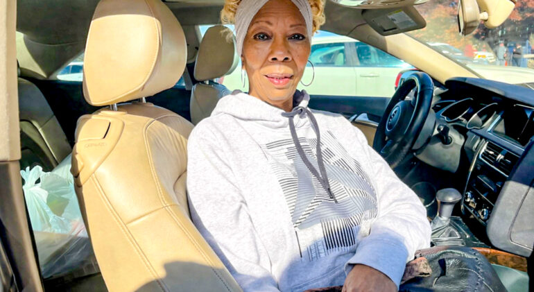 Black woman siting in car smiling wearing grey hoodie