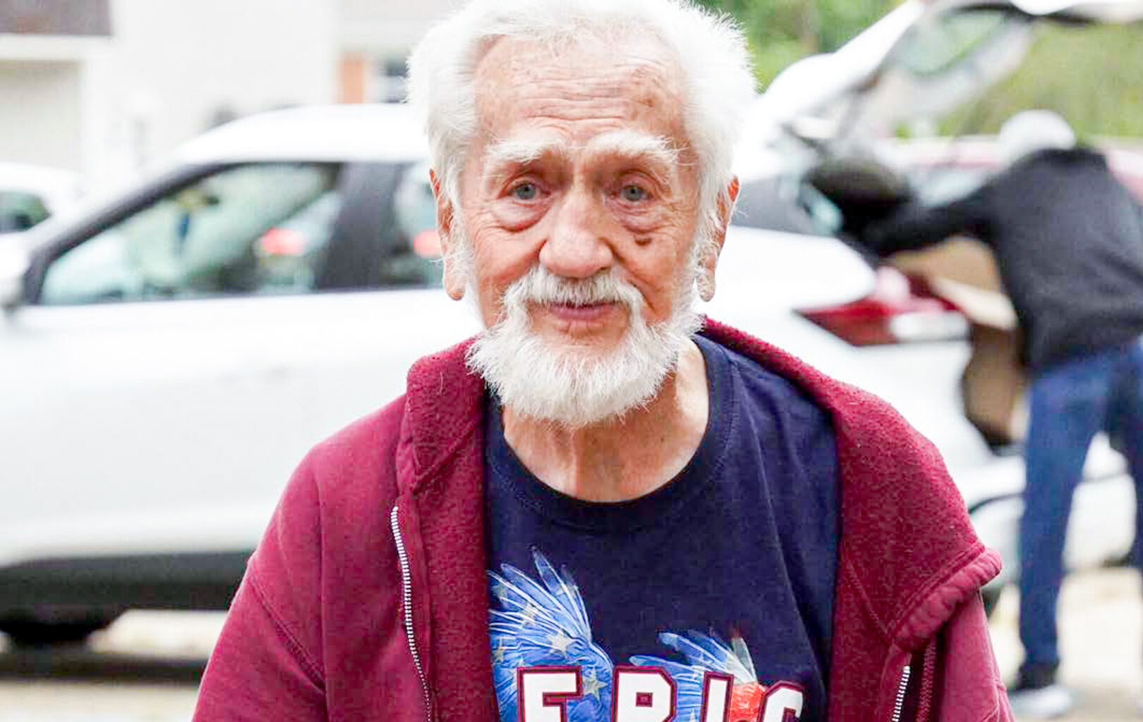 White old man wearing blue America shirt and red jacket