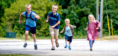 4 white kids running with back packs on smiling