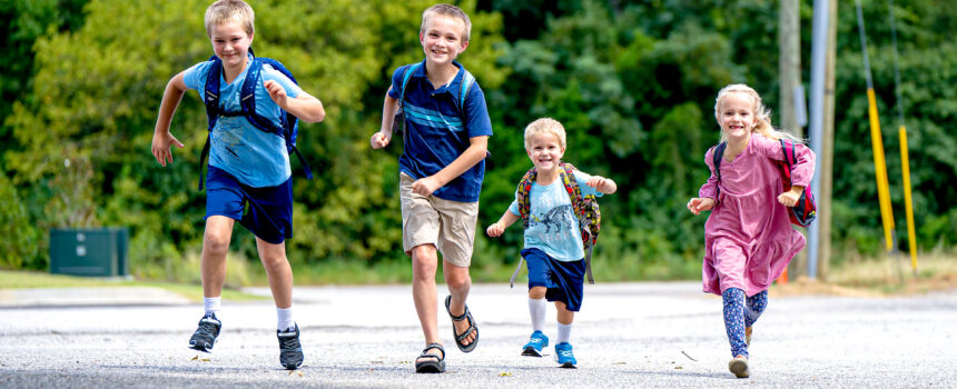 4 white kids running with back packs on smiling