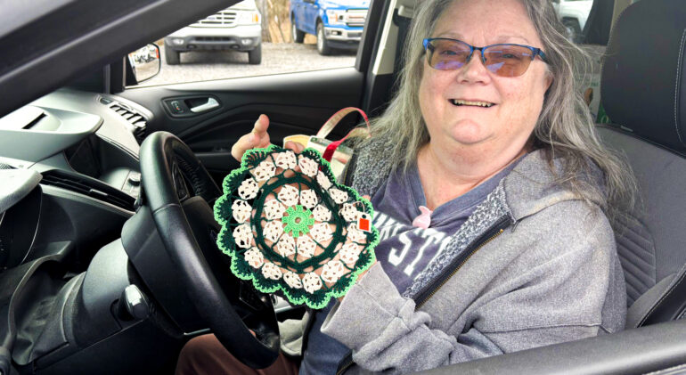 White old lady with grey hair and grey sweatshirt smiling in her car