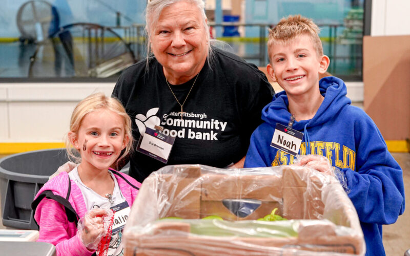 a boy wearing a blue hoodie and a girl wearing a pink shirt smiling with an older women wearing a black shirt