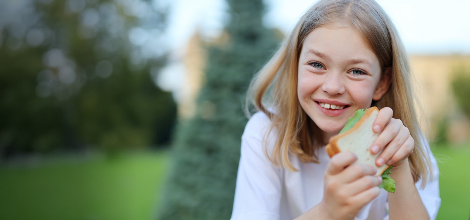 Young white child with blonde hair smiling holding food in a white shirt